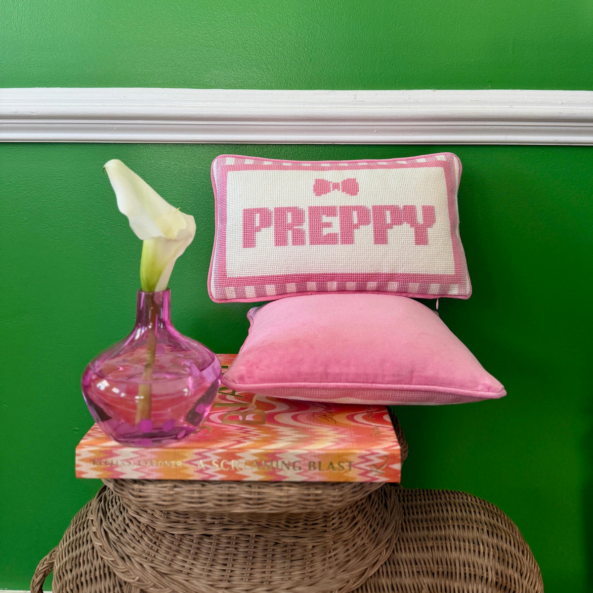 Pink 'PREPPY' pillow on a wicker stool with a green background