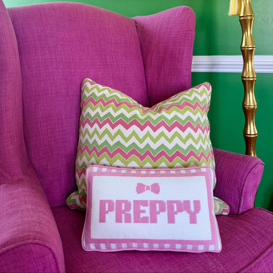 Pink armchair with a colorful zigzag pillow and a 'PREPPY' pillow against a green wall.